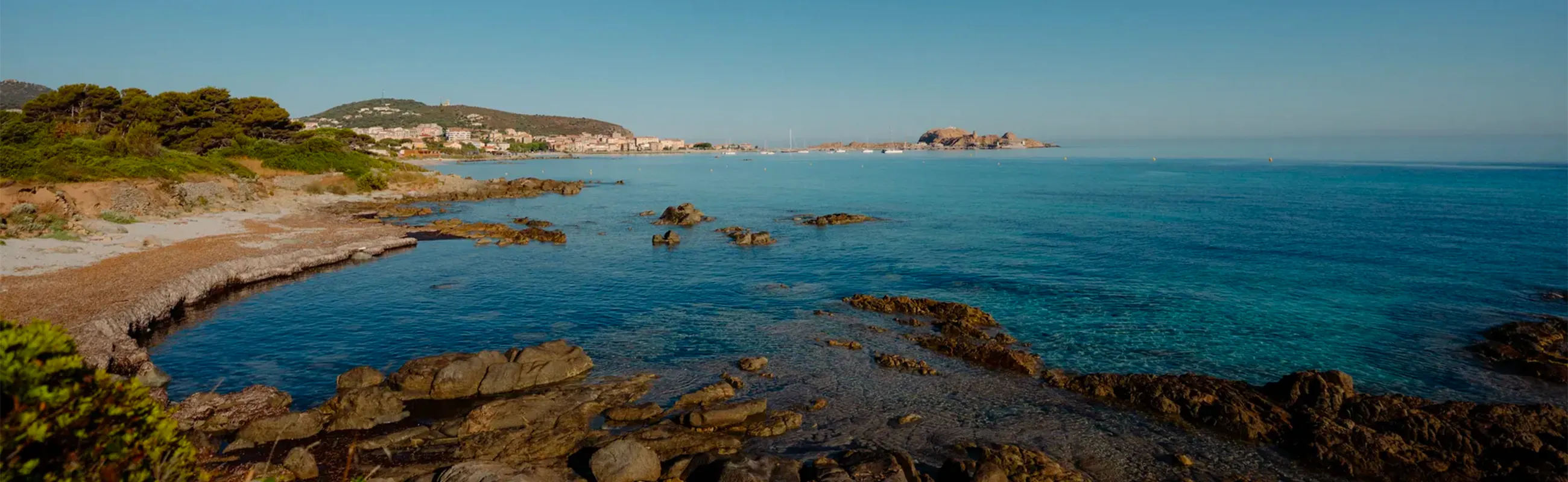 Vue panoramique de la côte rocheuse et de la mer turquoise en Balagne sous un ciel bleu.